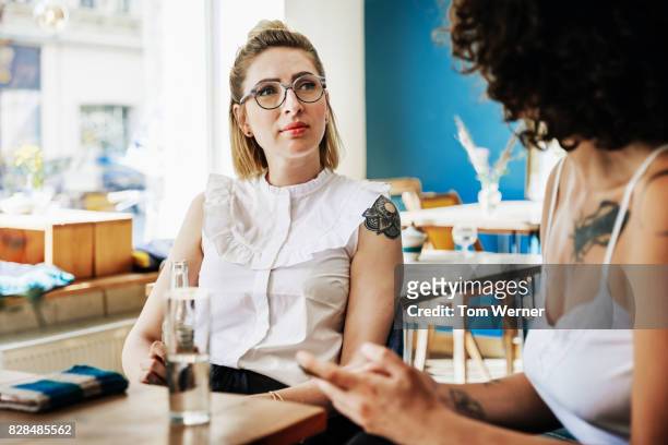 two stylish young women having conversation together in cafe - 2017 review stock-fotos und bilder