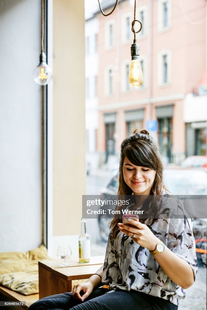 Stylish Young Woman Looking At Smartphone In Cafe