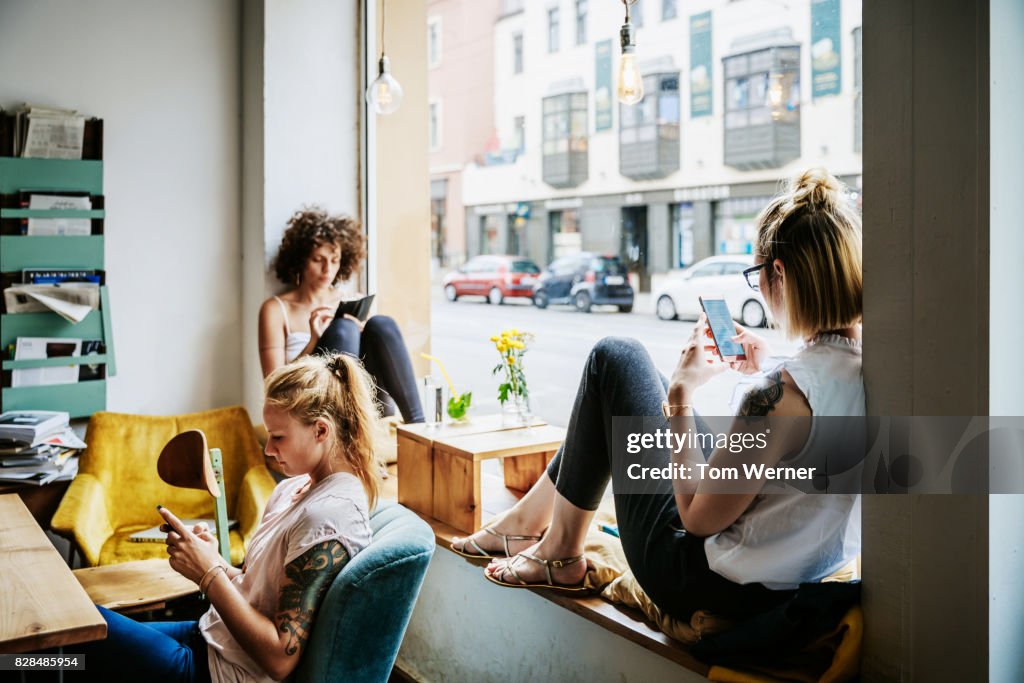 Young Women Relaxing In Cafe Using Their Smartphones