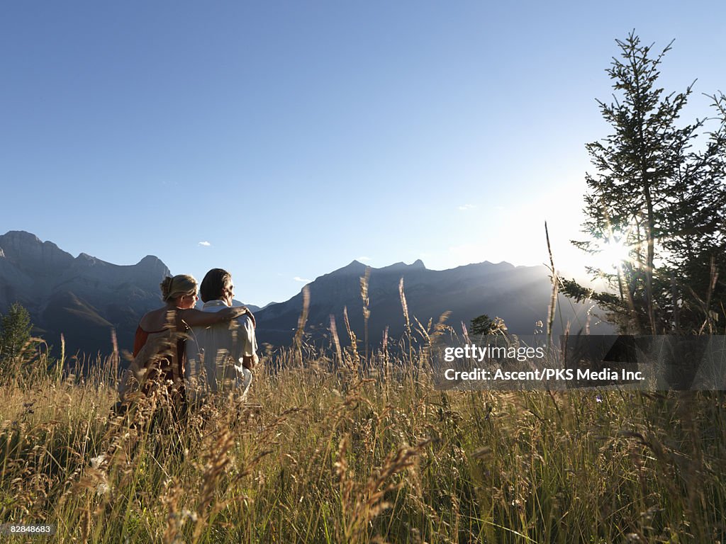 Couple sits in grassy mountain meadow at sunset