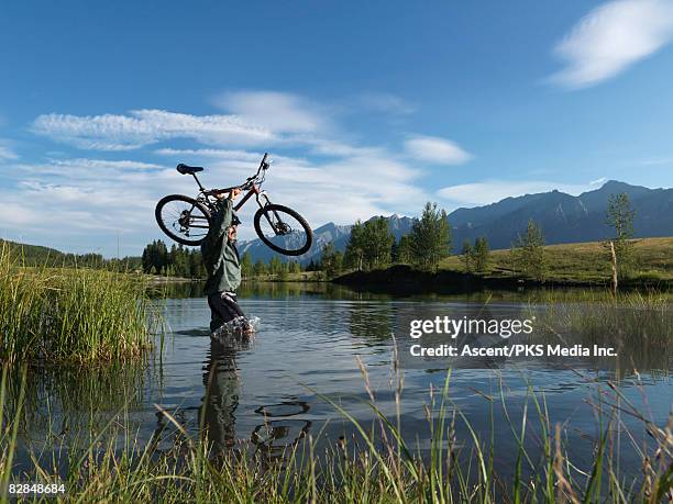 mountain biker crosses marsh with bike overhead - joint effort stock pictures, royalty-free photos & images