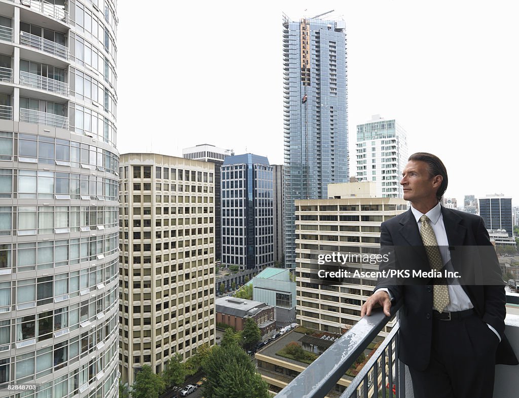 Businessman looks off deck of high rise in city