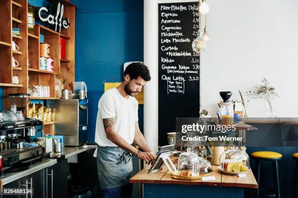 young waiter using tablet to manage orders at cafe counter - bar man t shirt stock-fotos und bilder