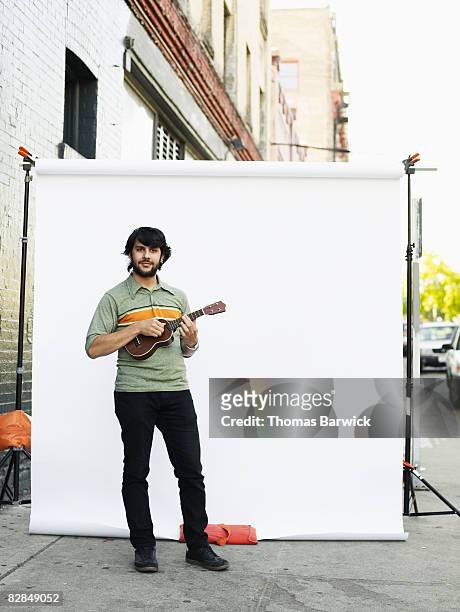 man standing on street playing ukulele - ukulele stock-fotos und bilder