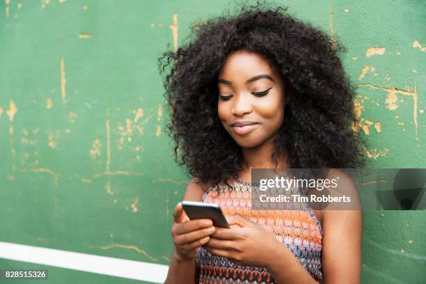 woman using smart phone next to green wall - sleeveless top stock pictures, royalty-free photos & images