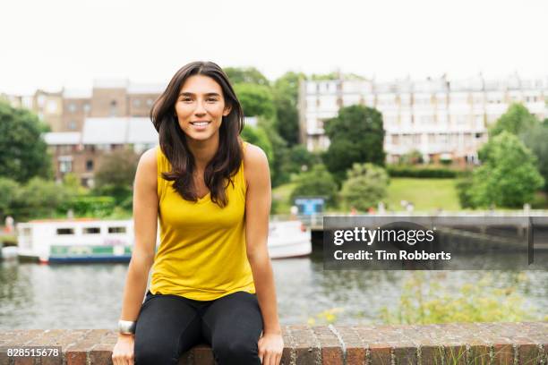 woman looking at camera sat on wall - geel hemd stockfoto's en -beelden