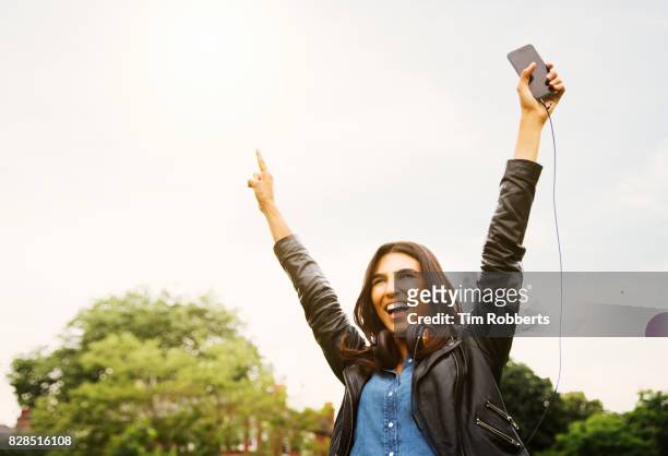 woman with arms in the air holding smart phone - freedom on festival stock-fotos und bilder