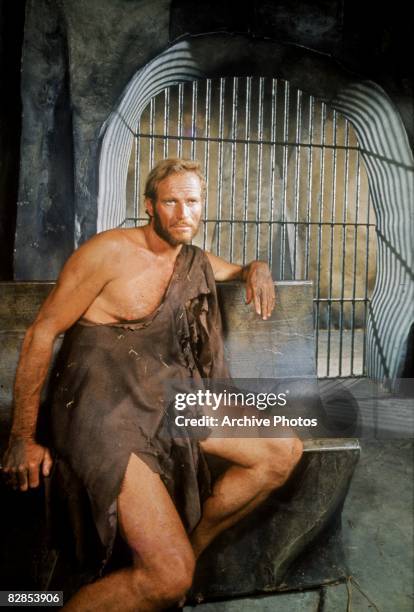 American actor Charlton Heston, dressed in rags, sits on a stone bench in jail in a still from the film, 'Planet of the Apes,' directed by Franklin...