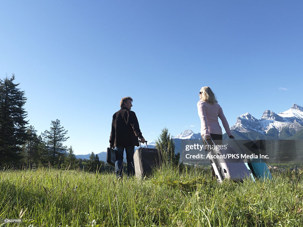 Couple walk with baggage through mountain meadow