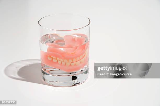 dentures in a glass of water - dentadura postiza fotografías e imágenes de stock