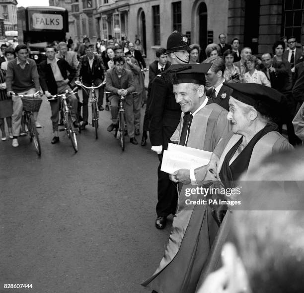 Cyclists come to a halt and people on the busy pavements pause to watch as recipients of Oxford University honourary degrees leave the Town Hall,...