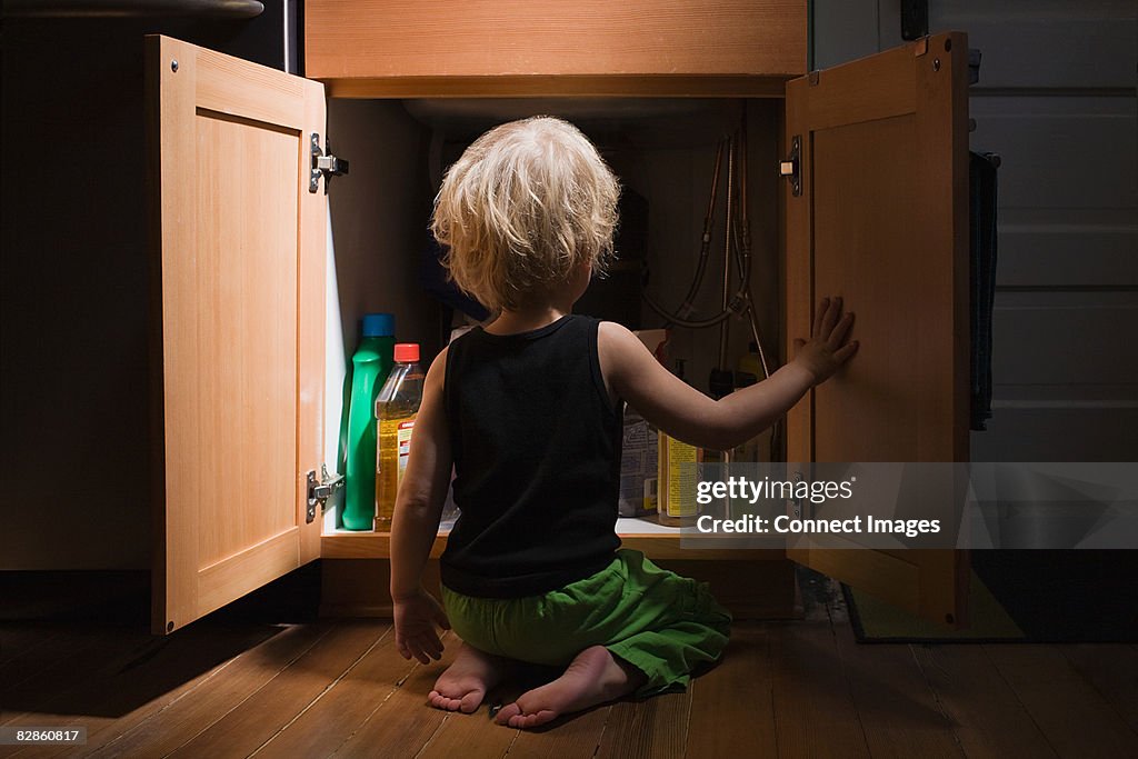 Little boy opening cupboard of cleaning products