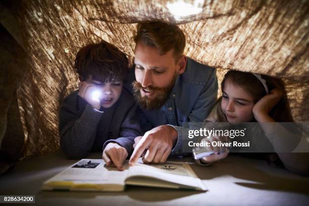 father reading book to children under a cloth - flashlight stock-fotos und bilder