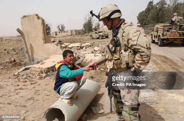 Soldier shakes hands with a curious Iraqi boy at the Iraq border with Kuwait as they both watch the arrival of one of the first shipments of water,...