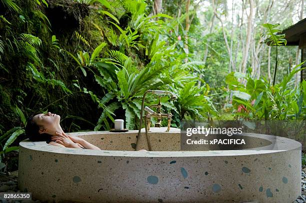 a  women relaxes in an outdoor bath tub. - bali spa stock pictures, royalty-free photos & images