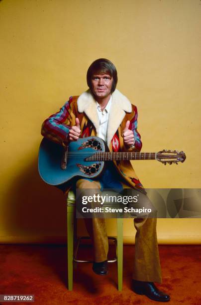 American musician Glen Campbell gives two thumbs up as he sits in front of a yellow backdrop, Los Angeles, California, 1978.