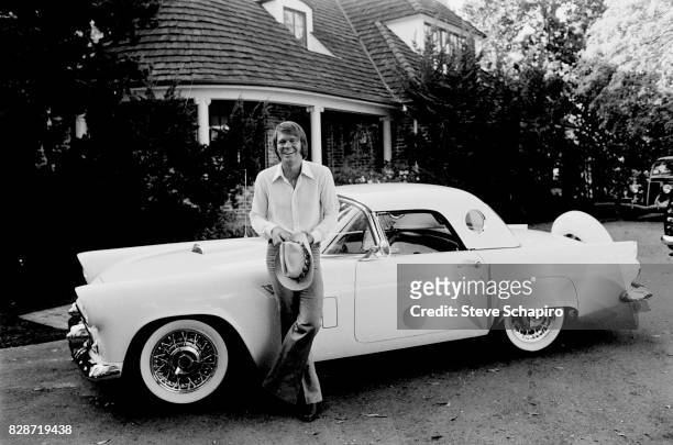 Portrait of American musician Glen Campbell as he smiles and leans against his car, a 1956 Ford Thunderbird, in the driveway of his home, Los...