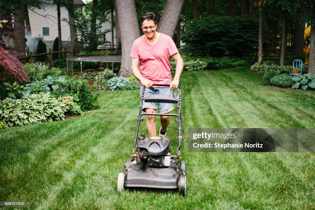 Smiling older man mowing the lawn in a backyard