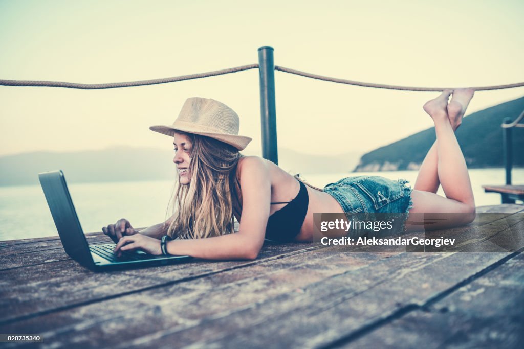 Young Smiling Female Surfing the Net on Lake Pier on Summer