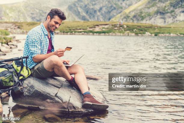 hombre de reclinación en el lago y compras en línea con tarjeta de crédito - red artículos deportivos fotografías e imágenes de stock