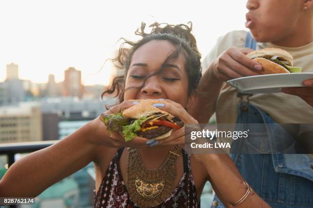 urban rooftop bbq - adults eating hamburgers stock-fotos und bilder
