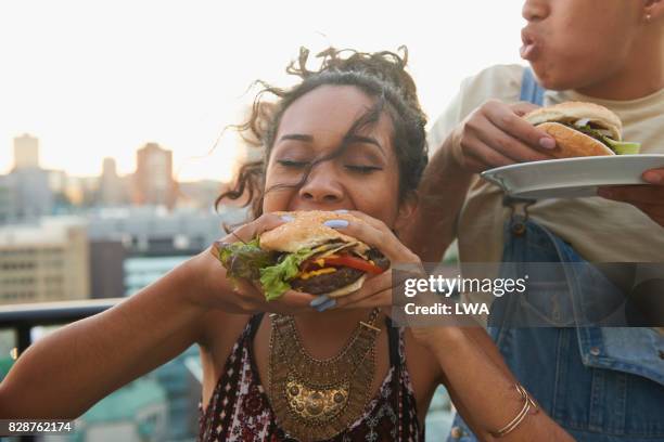 urban rooftop bbq - woman eating burger stockfoto's en -beelden