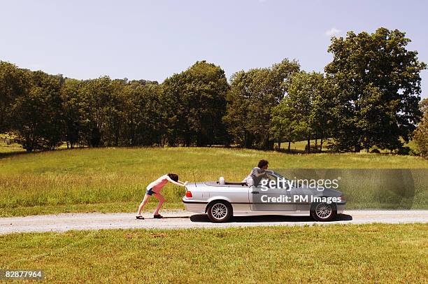 young couple pushing car along rural road - country road side stock pictures, royalty-free photos & images
