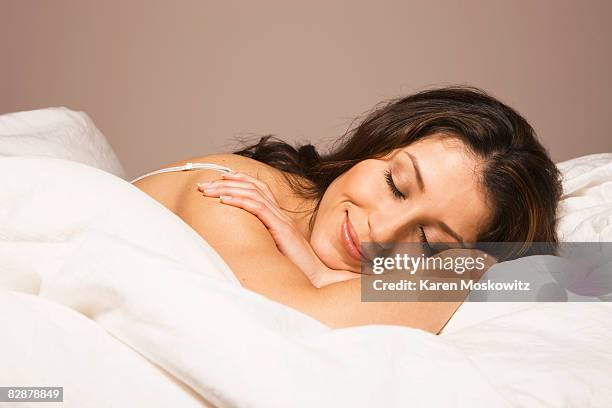 hispanic woman laying in bed smiling - woman in bed stock-fotos und bilder