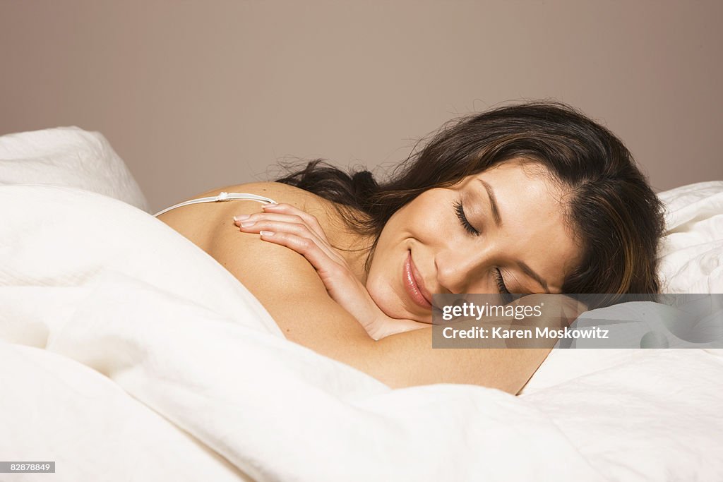 Hispanic woman laying in bed smiling
