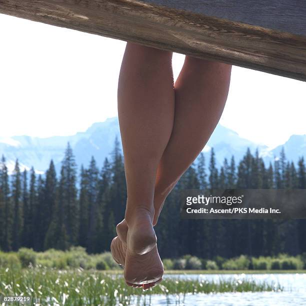 woman's legs dangle over edge of wharf - bergsteiger stockfoto's en -beelden