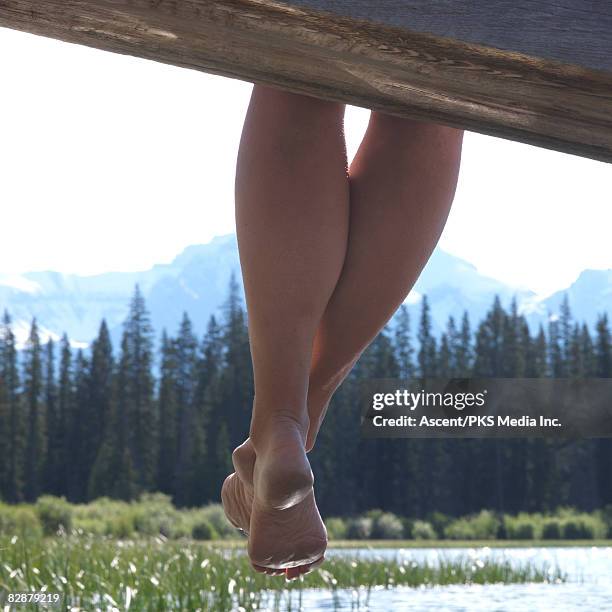 woman's legs dangle over edge of wharf - jetty stock pictures, royalty-free photos & images