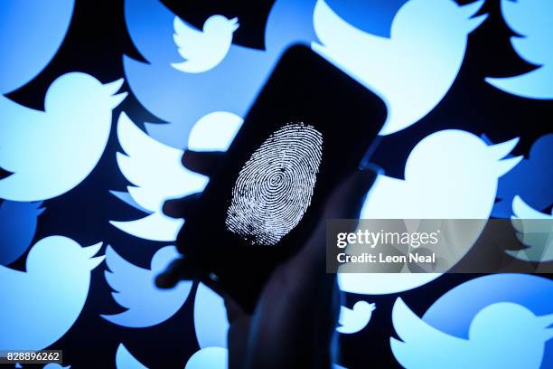In this photo illustration, a thumbprint is displayed on a mobile phone as the logo for the Twitter social media network is projected onto a screen...