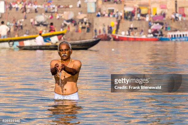 Man, pilgrim, is taking bath and praying on the sand banks at the holy river Ganges, panorama of Dashashwamedh Ghat, Main Ghat, in the distance.