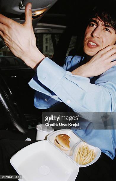young man eating in car while speaking with mobile phone - snacking on the go stock-fotos und bilder