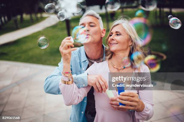 pareja juguetona soplar burbujas en el parque - bubbles happy fotografías e imágenes de stock