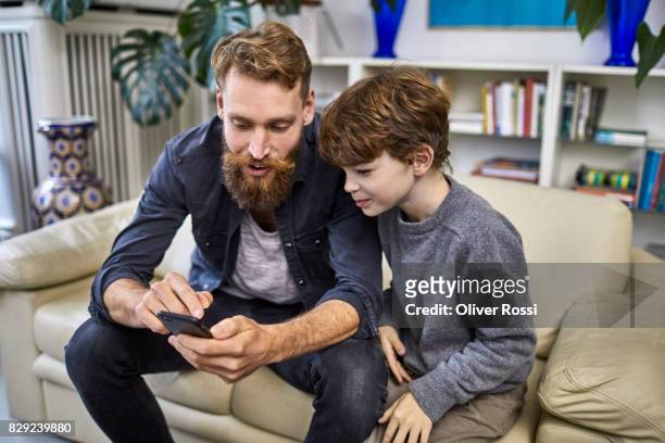 father and son with cell phone on sofa - tre quarti foto e immagini stock