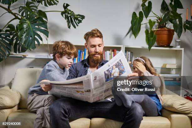 father with two children reading newspaper on sofa - topnews foto e immagini stock