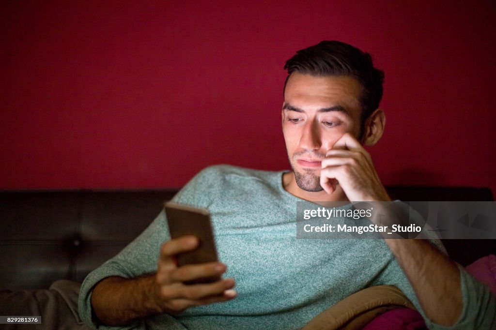 Thoughtful Man Using Smartphone on Sofa at Night