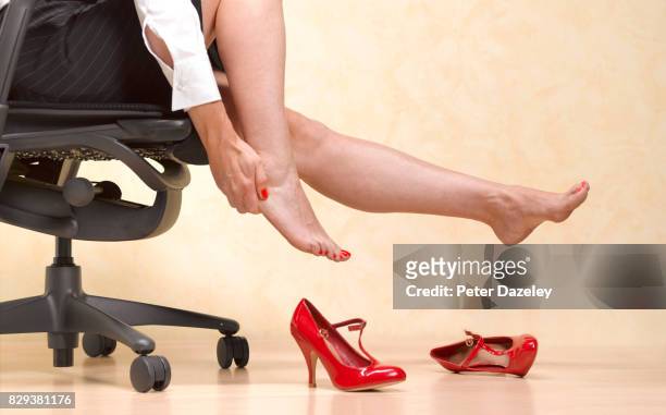 removing painful killer heels to massage feet in office - high heel stockfoto's en -beelden
