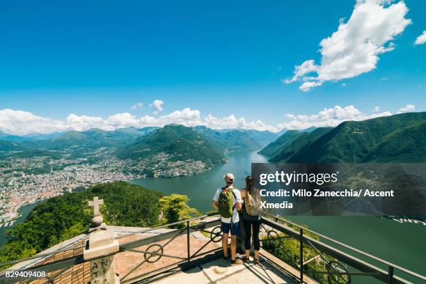 couple standing on viewpoint overlooking lake and mountains - schweiz stadt landschaft stock-fotos und bilder