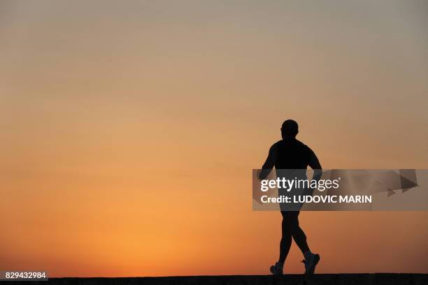 Man jogs at sunset along the coast in the village of Marzameni, south east Sicily on August 9, 2017.