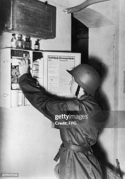 Female air raid warden checks the contents of a household first aid cupboard, Germany, circa 1938. Exact regulations, specifying what it should...