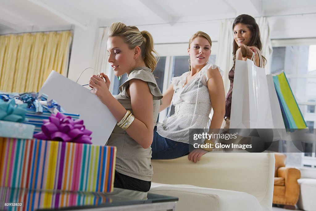 Young woman checking her shopping bags with her friends in the background