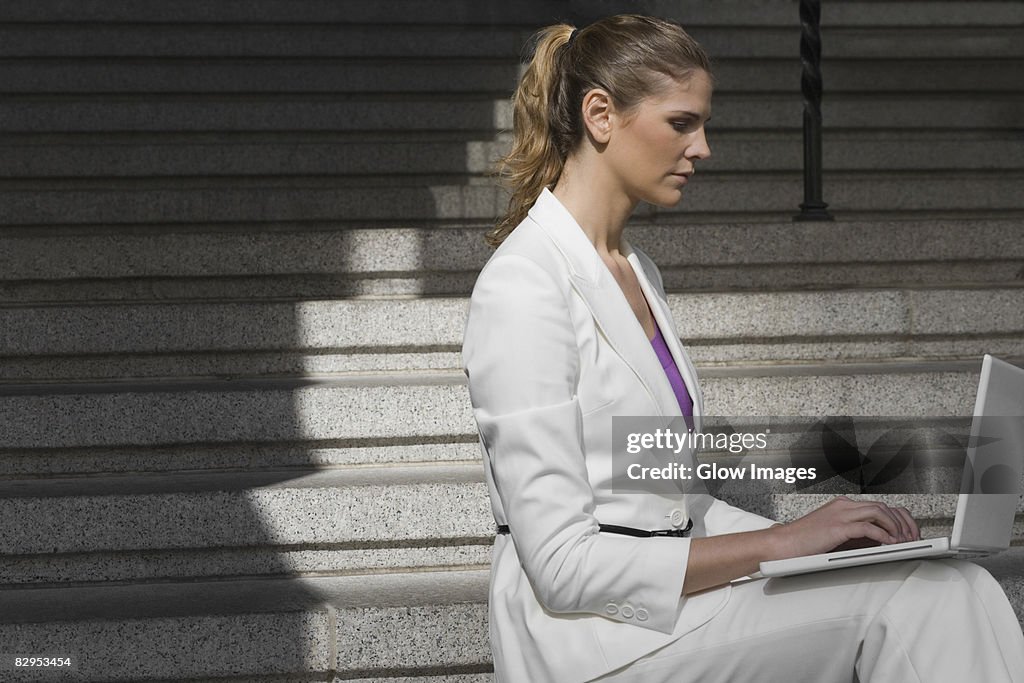Side profile of a businesswoman sitting on a staircase and using a laptop