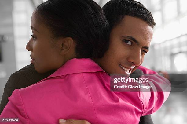 close-up of a businessman embracing a businesswoman and winking at an airport - flirting stock pictures, royalty-free photos & images