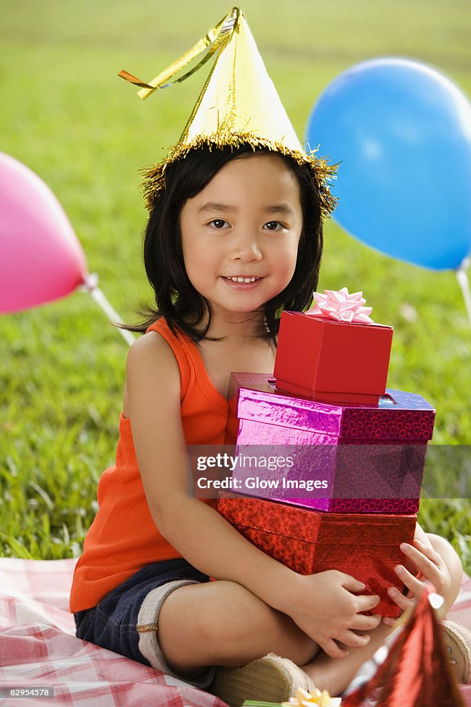 Portrait of a girl with holding a stack of birthday gifts and smiling in a park