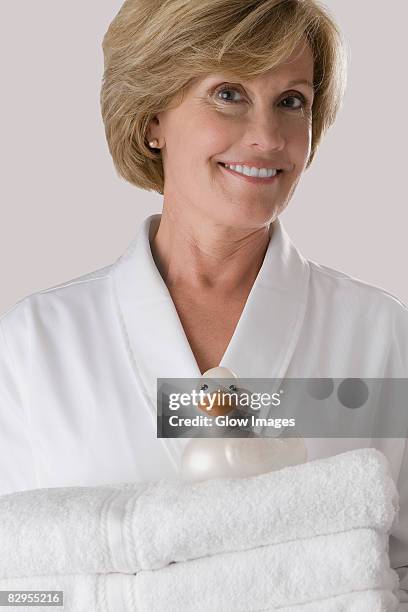 portrait of a mature woman holding a stack of folded towels - une seule femme d'âge mûr photos et images de collection