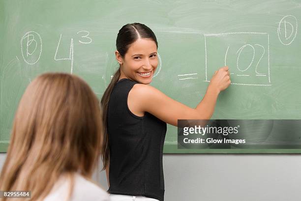 female teacher teaching a schoolgirl in a classroom and smiling - two female teachers blackboard stockfoto's en -beelden