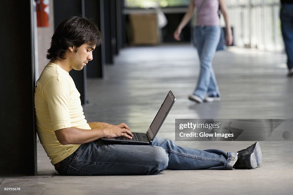 Side profile of a young man using a laptop in a corridor