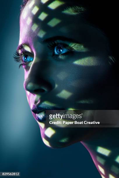 portrait of a woman hiding under a textured ceiling that forms different shapes and sizes of shadows that are reflected on her face - solo una donna giovane foto e immagini stock